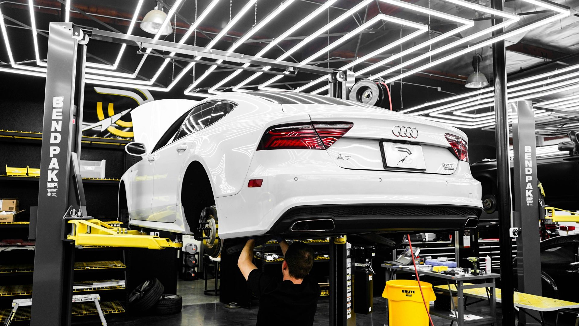 Ein weißer Luxuswagen wird in einer modernen Werkstatt von einem Mechaniker gewartet.